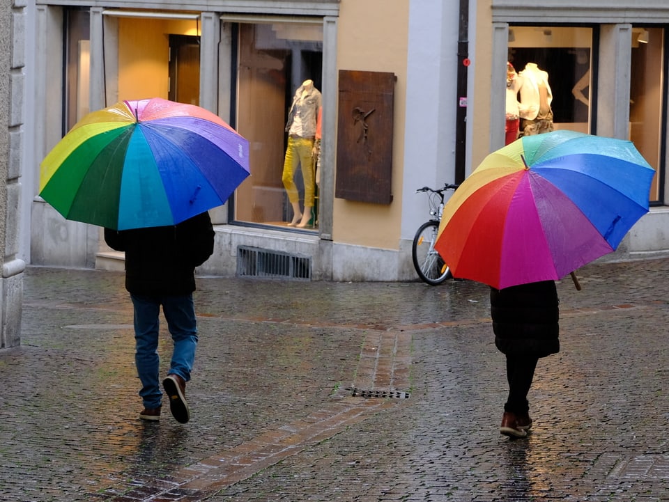 Zwei Schirmträger in der Stadt von hinten fotografiert.