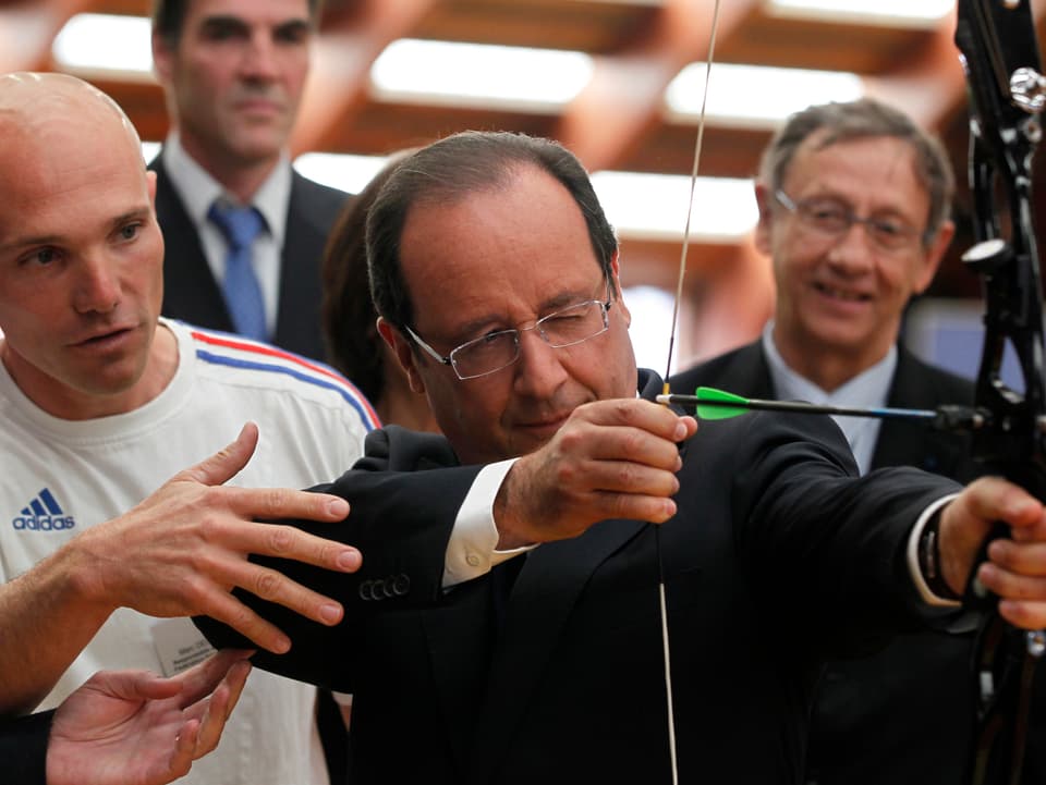 Francois Hollande hält einen Bogen in der Hand und zieht an der Sehne.