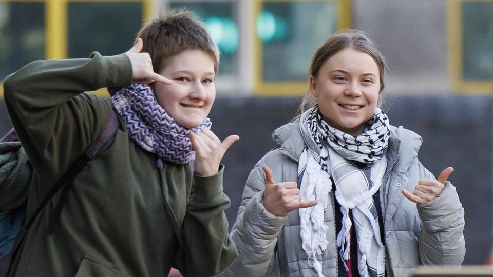 Zwei junge Frauen schauen vergnügt in die Kamera und formen Zeichen mit ihren Fingern
