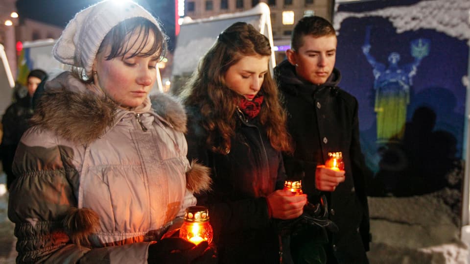 Zwei junge Frauen und ein junger Mann gedenken mit Kerzen in der Hand der toten Soldaten.