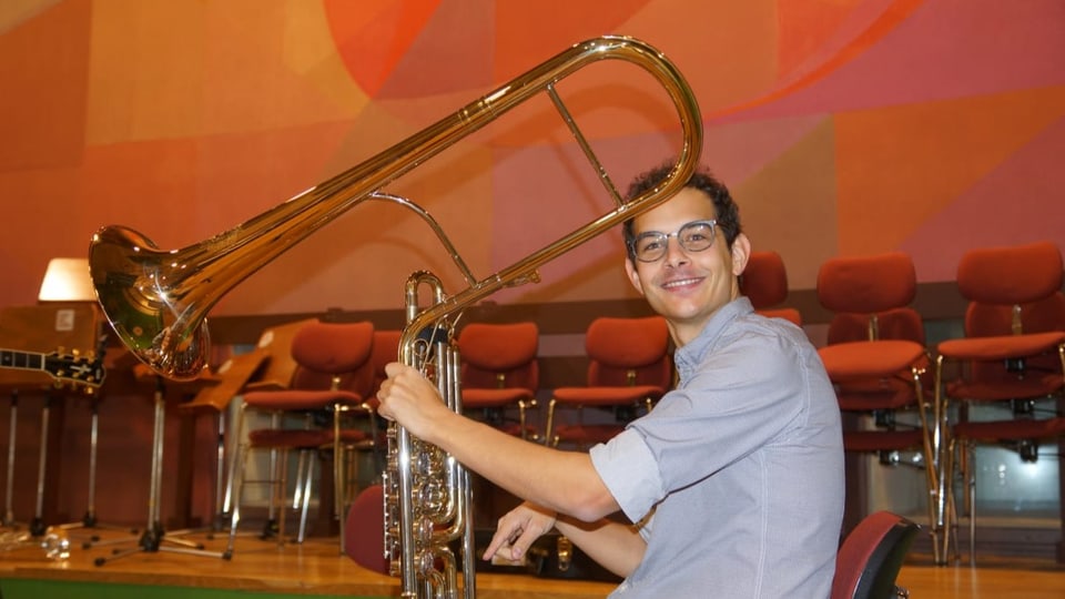 Musiker hält ein Blechblasinstrument in der Hand das über einen Meter lang ist.