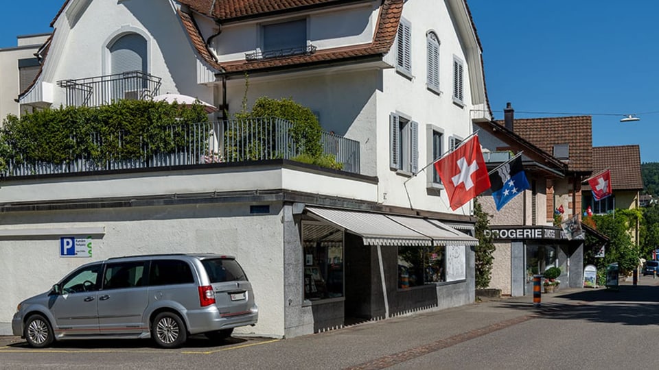 Strassenansicht mit Ladengeschäften in älteren Häusern, es wehen Schweizer und Aargauer Fahnen.