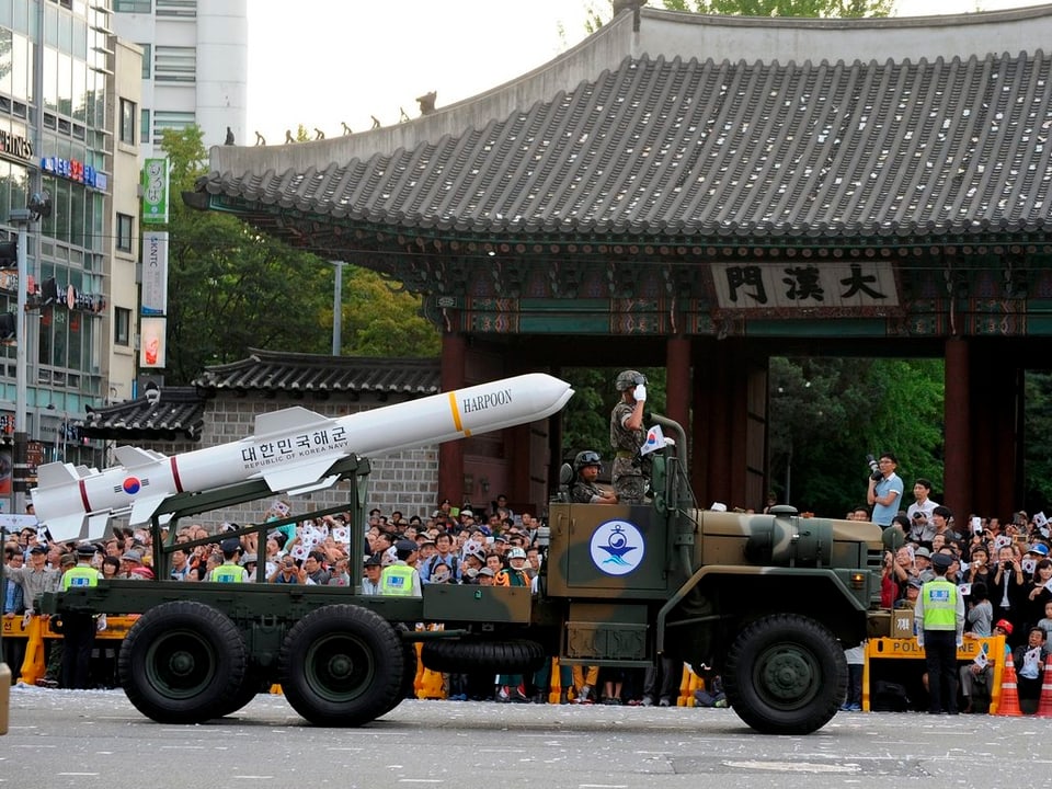Eine weisse Rakete, die auf einem Träger transportiert wird. Eine Menschenmenge begeisterter Südkoreaner besichtigt dieses Spektakel. 