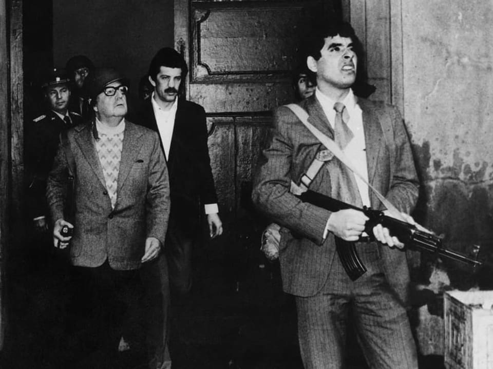 Bild in schwarz/weiss. Allende schreitet aus einer Tür des Präsidentenpalasts. Er ist umgeben von bewaffneten Soldaten und Männern in Anzügen.