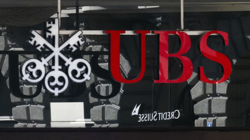 Logo der UBS an einem Gebäude, darin spiegelt sich klein das Logo der CS