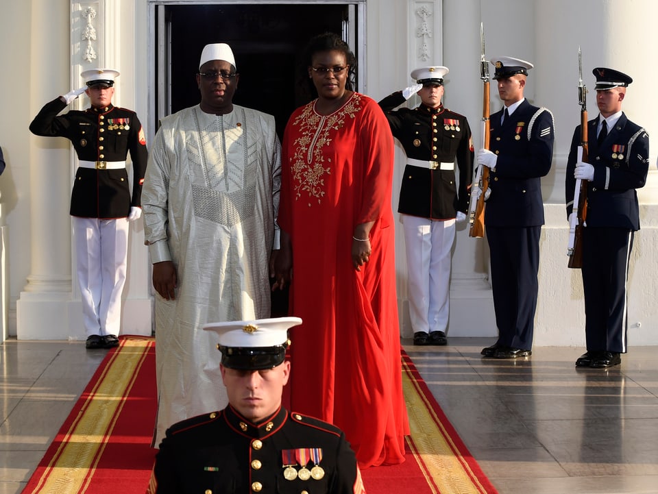 Sall und Ehefrau in traditionellen Kleidern auf dem roten Teppich unter den Augen der Ehrengarde.