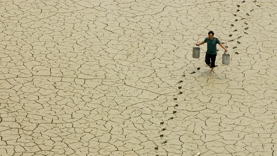 Chinesischer Bauer schleppt Kübel mit Wasser über ausgedörrte Erde. 