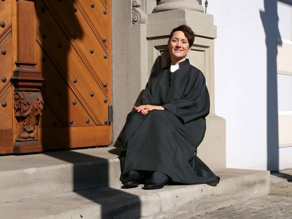 Junge Pfarrerin sitzt auf einer Treppe vor einem Kircheneingang