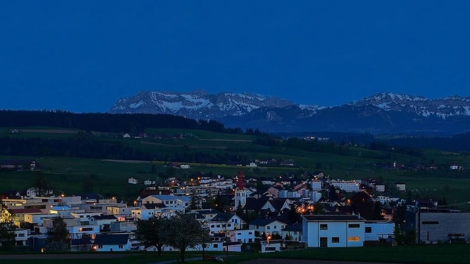 Dorf in der Nacht mit Kirche und Berg im Hintergrund.