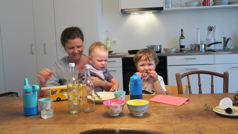 Eine junge Mutter mit zwei Kindern an einem Küchentisch beim Essen. 
