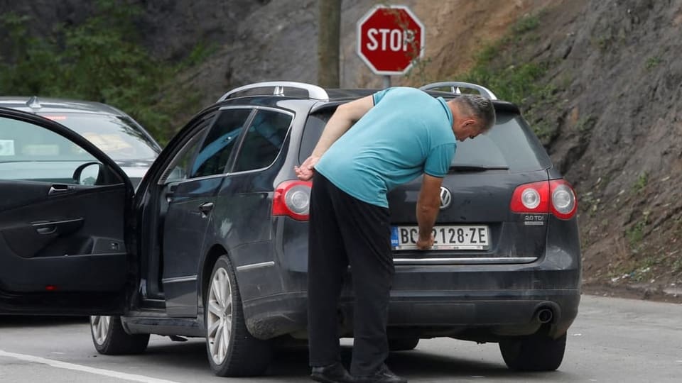 Ein Mann wechselt sein serbisches Nummernschild an seinem schwarzen Volkswagen.