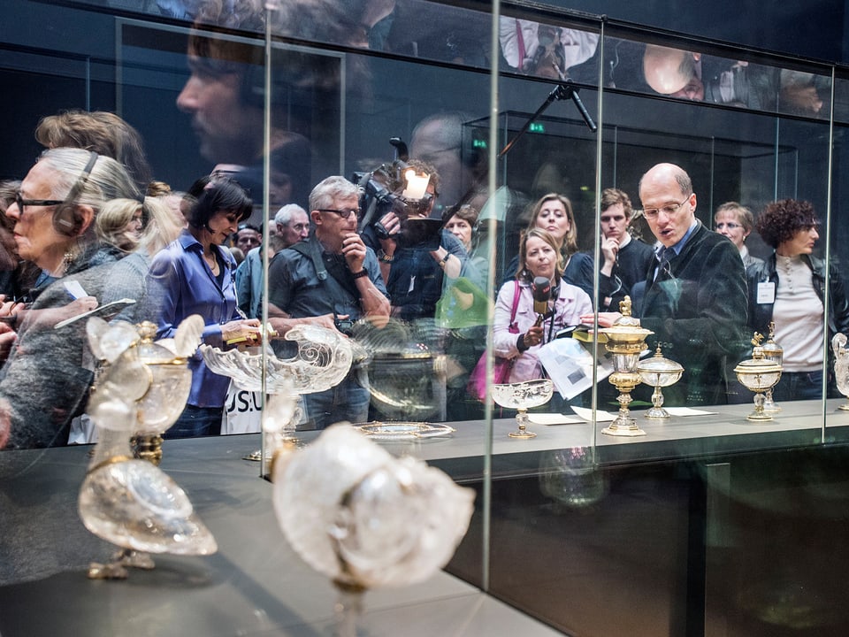 Elsbeth Gugger mit Alain de Botton und vielen anderen Journalisten hinter einer Museumsvitrine.