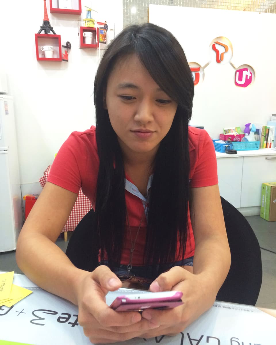Eine koreanische junge Frau schaut auf ein rosafarbenes Smartphone.