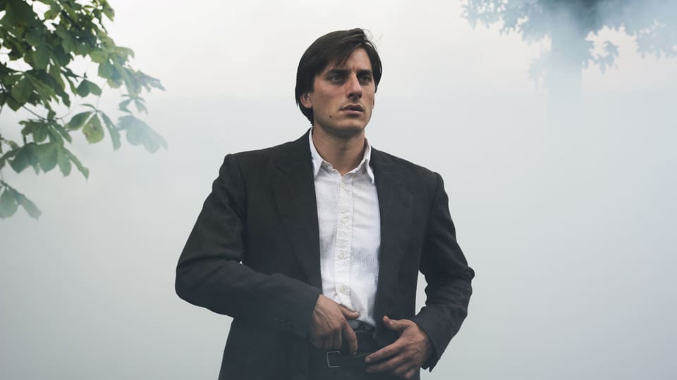 Ein junger Mann steht im Nebel, die Hand an einer Pistole, die in seinem Hosenbund steckt.