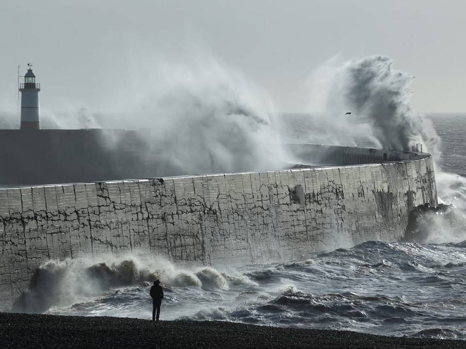 Eine Person beobachtet, wie eine riesige Welle den Hafenwall in Newhaven trifft.
