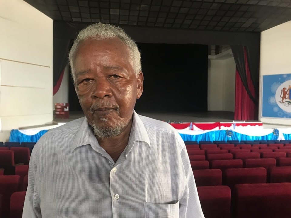 Theaterdirektor Abdikadir Abdi Yusuf steht im Theatersaal vor roten Samtsitzen.
