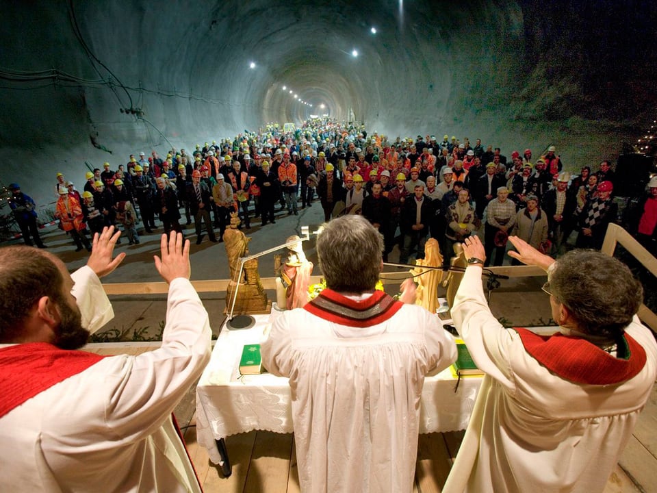 Ein Gottesdienst im Tunnelinnern mit drei Pfärrer im Vordergrund, dahinter zahlreiche Bauarbeiter. 