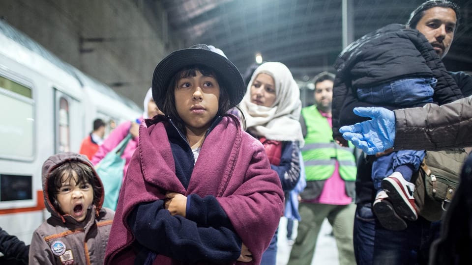 Flüchtlingsfamilie auf einem Bahnhof in Deutschland, links im Bild ein Zug