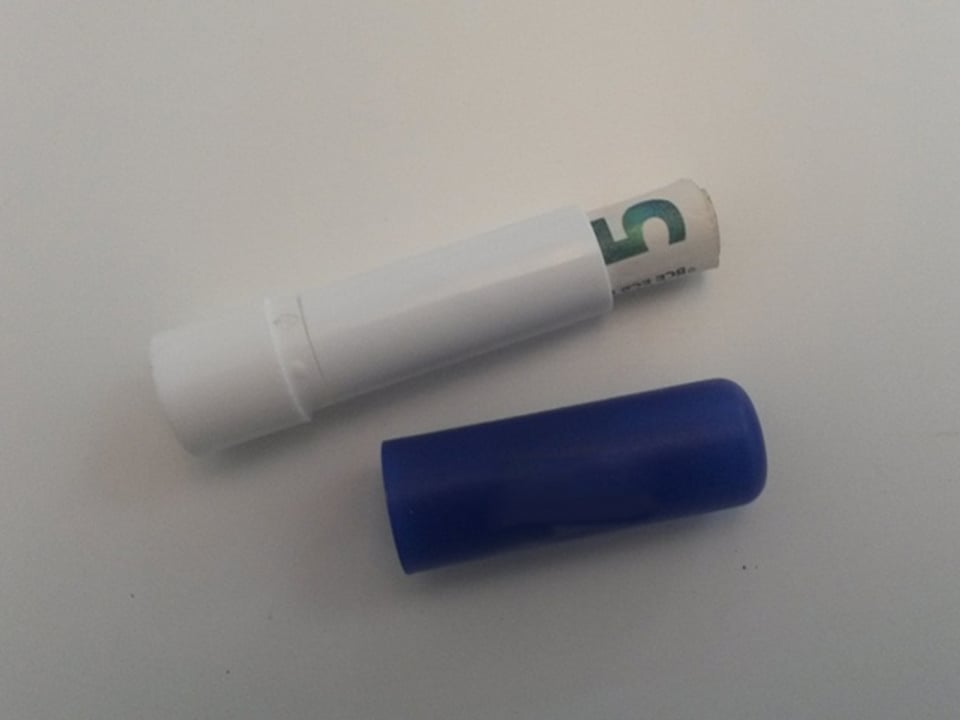 Geöffneter Lippenpomaden-Stift mit einer Geldnote darin.