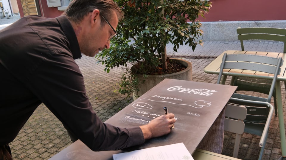 Mann schreibt auf Tafel Mittagsmenue auf