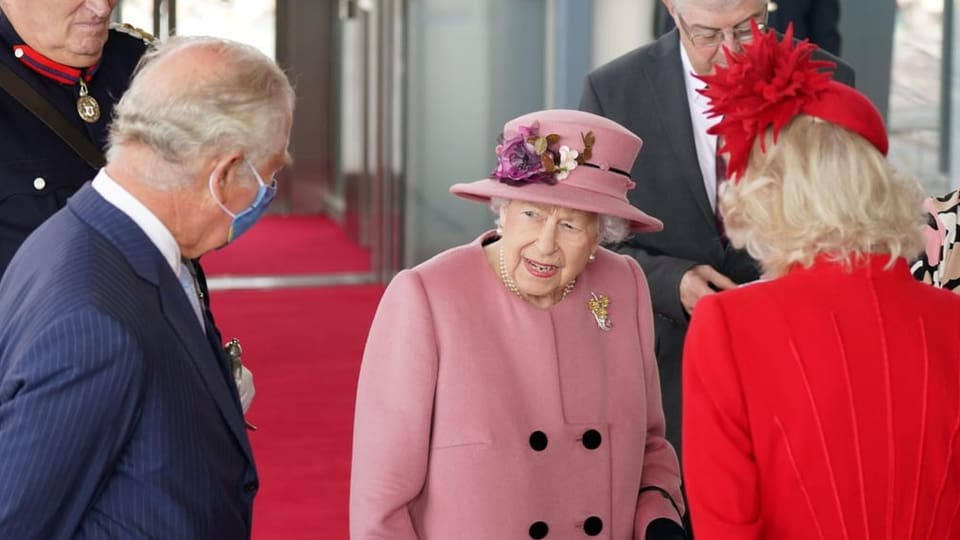 Die Queen in einem rosa Doppelreiher mit Hut, Charles im Anzug und Camilla im roten Kleid mit Hut.