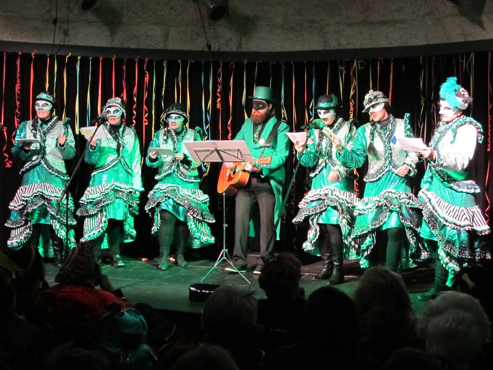 Frauen in grünen Fasnachtskostümen mit Mann an Gitarre. 
