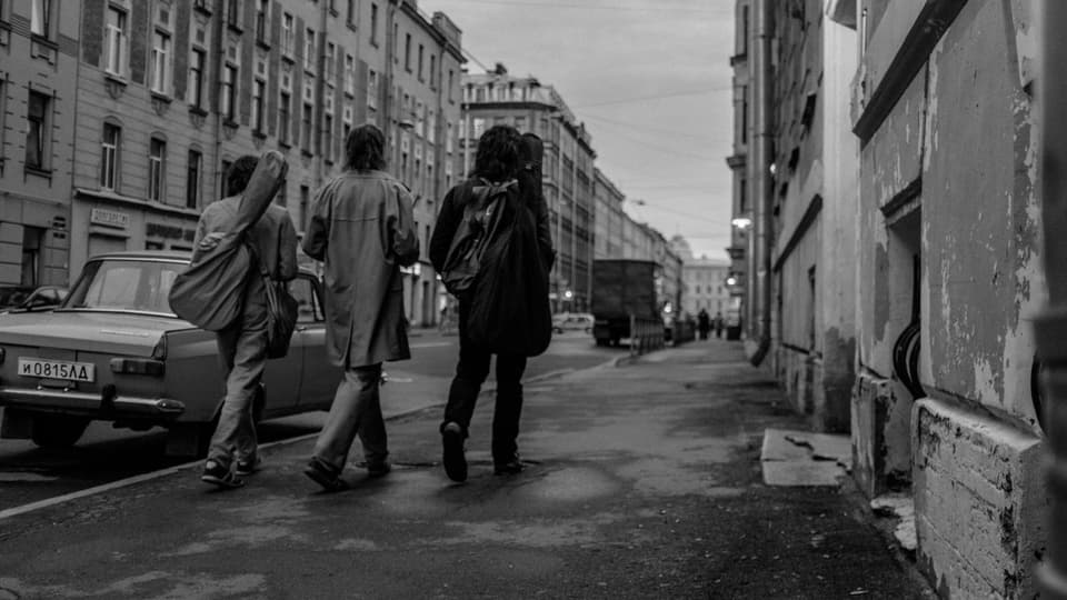 Drei Männer mit Gitarren gehen eine Strasse runter, schwarzweiss Filmstitt
