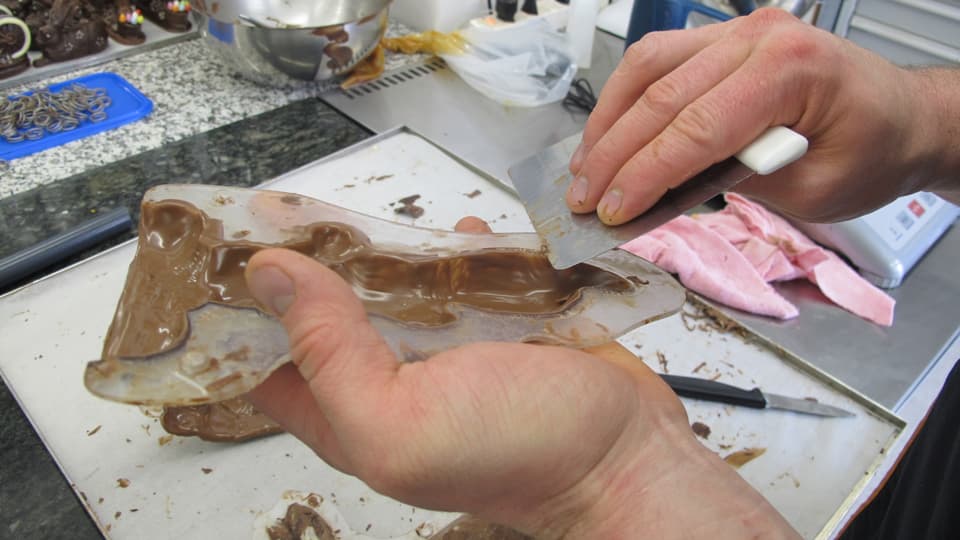 Von Hand wird mit einem Messer die überflüssige Schokolade von den Plastikformen gekratzt.