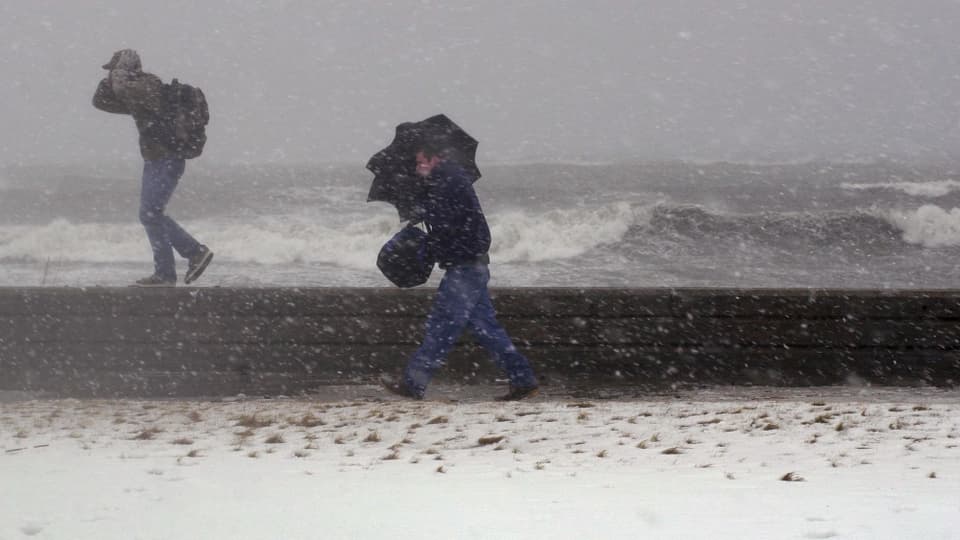 Zwei Männer laufen bei stürmischen Verhältnissen an der Ostküste der USA. Im Hintergrund das aufgewühlte Meer.