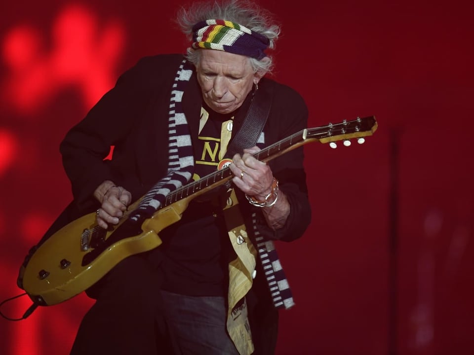 Keith Richards spielt Gitarre vor rotem Hintergrund