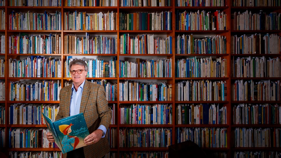 Ein Mann steht mit einem Buch vor einem riesen Bücherregal.