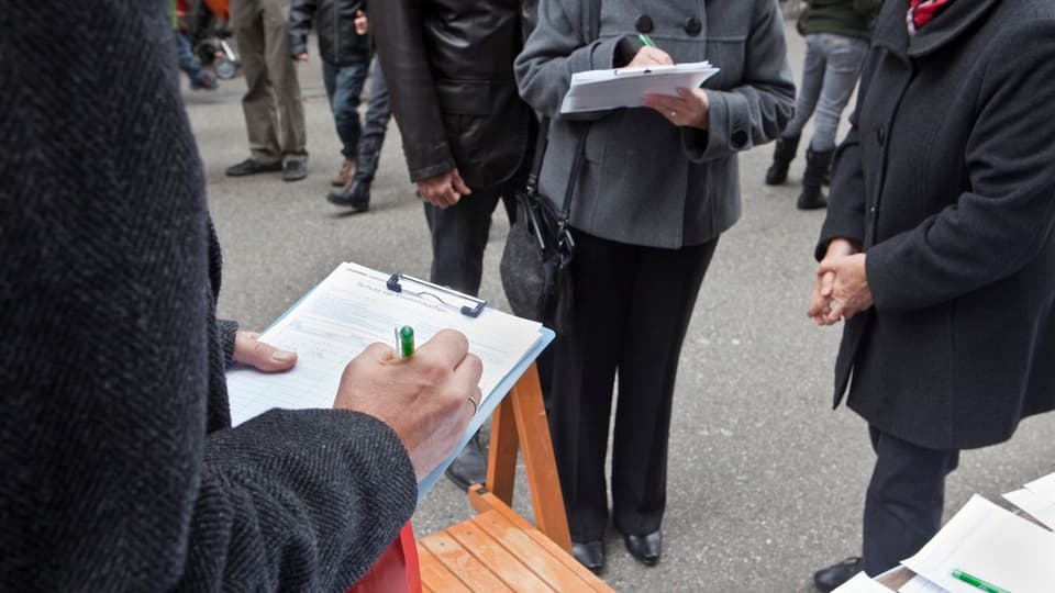 Unbekannte Menschen füllen auf einer Strasse Unterschriftenbögen für eine Volksinitiative aus.