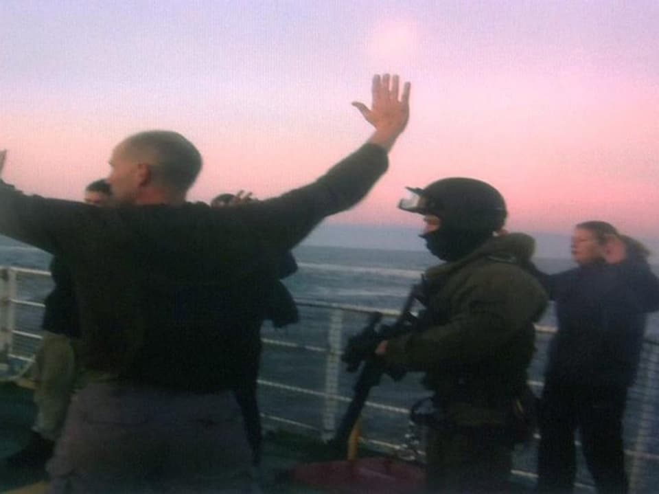 Ein vermummter und bewaffneter Soldat sowie Aktivisten mit erhobenen Händen