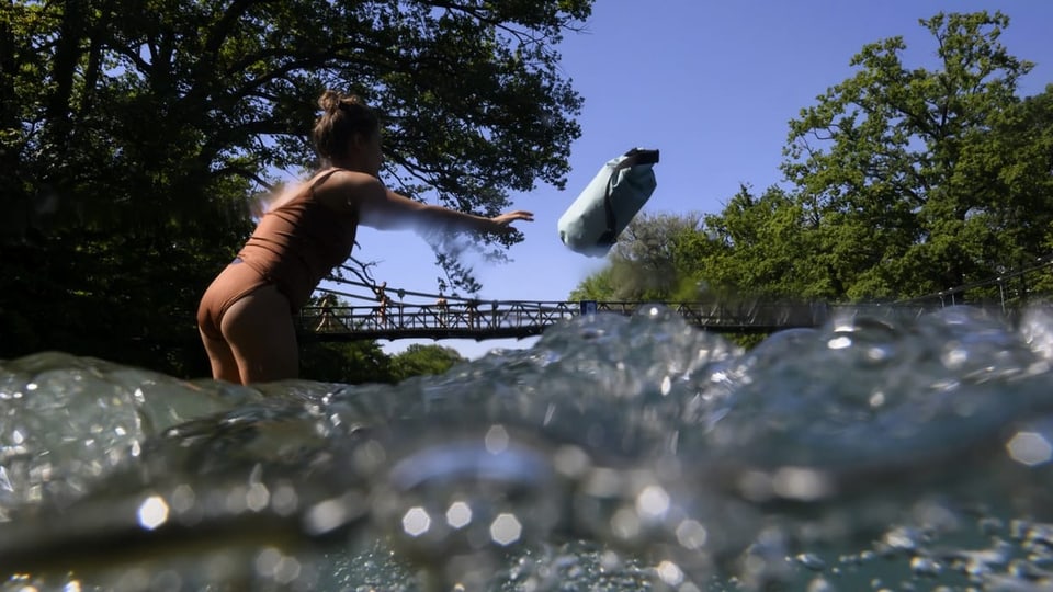 Auf dem Bild ist eine Frau zu sehen, die einen Schwimmsack in den Fluss wirft.