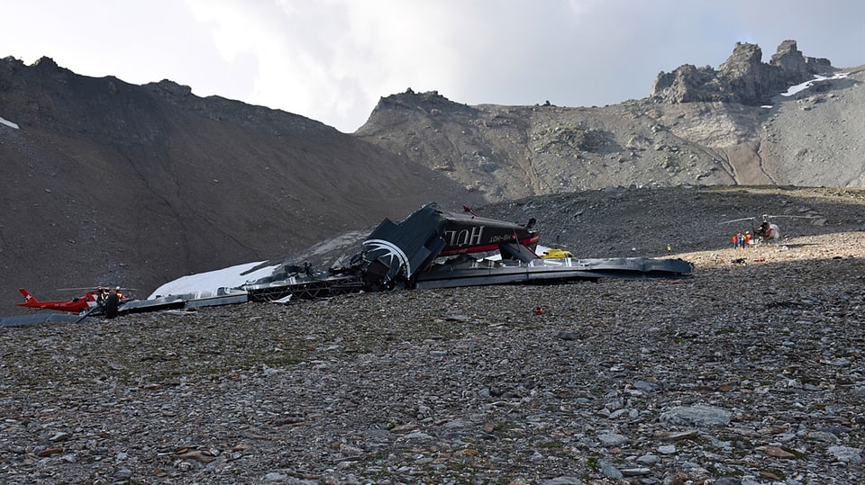 Flugzeugwrack vor Bergkulisse, im Hintergrund ist ein Helikopter sichtbar.