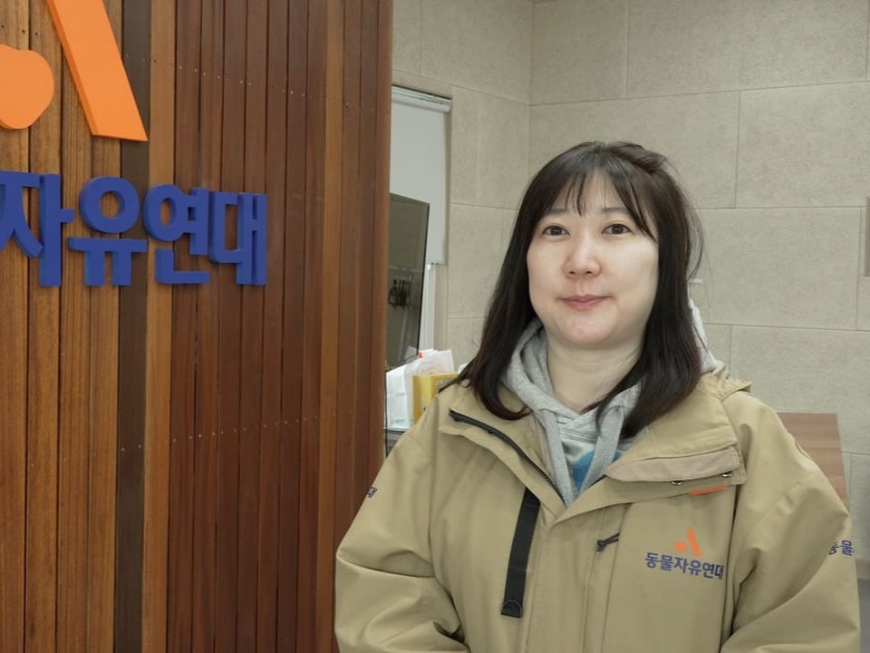 Frau in beiger Jacke vor einem Schild mit koreanischer Schrift