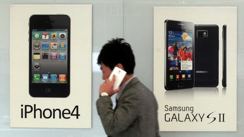 Eine Person geht an zwei Plakaten mit Samsung beziehungsweise Apple-Produkten vorbei.
