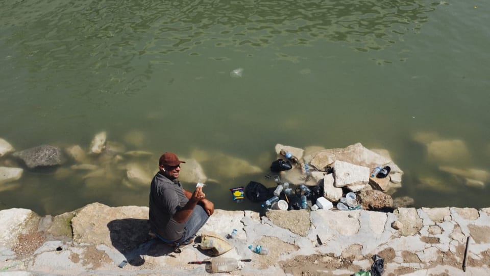 Ein Mann sitzt am Fluss. Dieser ist verschmutzt