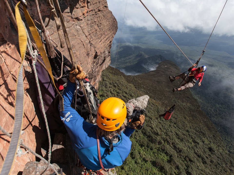 Ein Kletterer filmt an der Felswand, der andere hängt in der Luft.