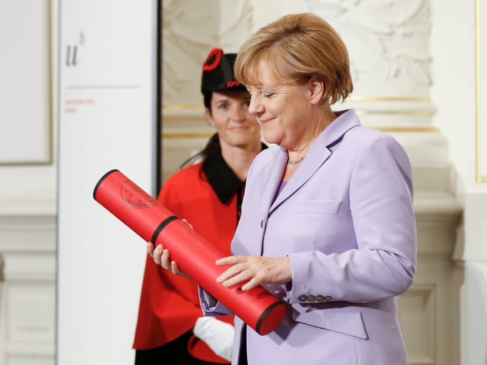 Angela Merkel mit einer roten Rolle, in welcher die Urkunde ist.