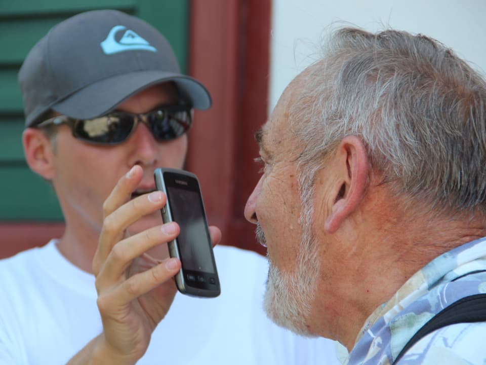 Reto Scherrer hält einem Interviewpartner sein Handy vor den Kopf um eine Aufnahme zu machen.