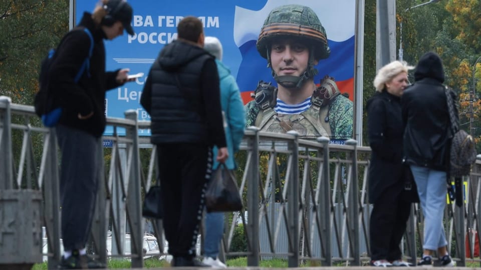 Plakat in St.Petersburg mit einem Soldatenporträt, davor Passanten.