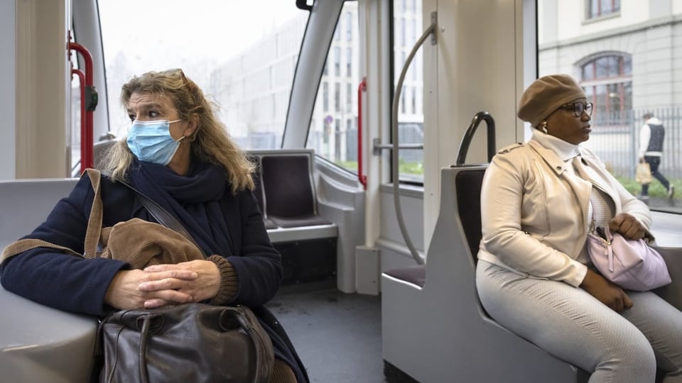 Zwei Pendlerinnen im Tram. Eine mit, die andere ohne Maske.