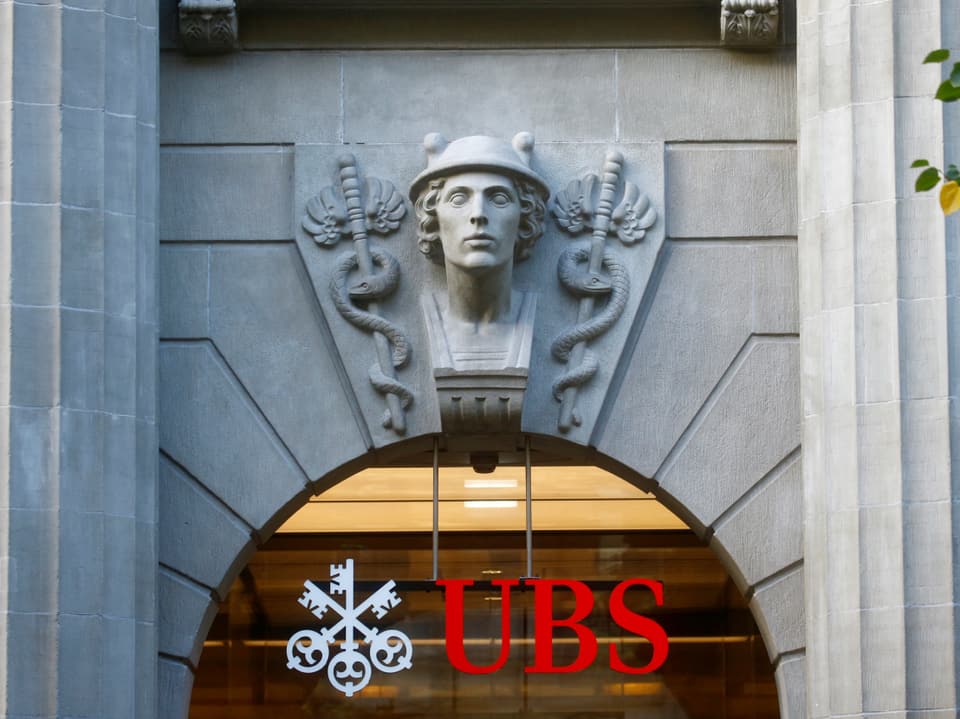 Aufnahme einer Fassade eines UBS-Gebäudes. Es ist das Banklogo und ein Stuck (Kopf) zu sehen.