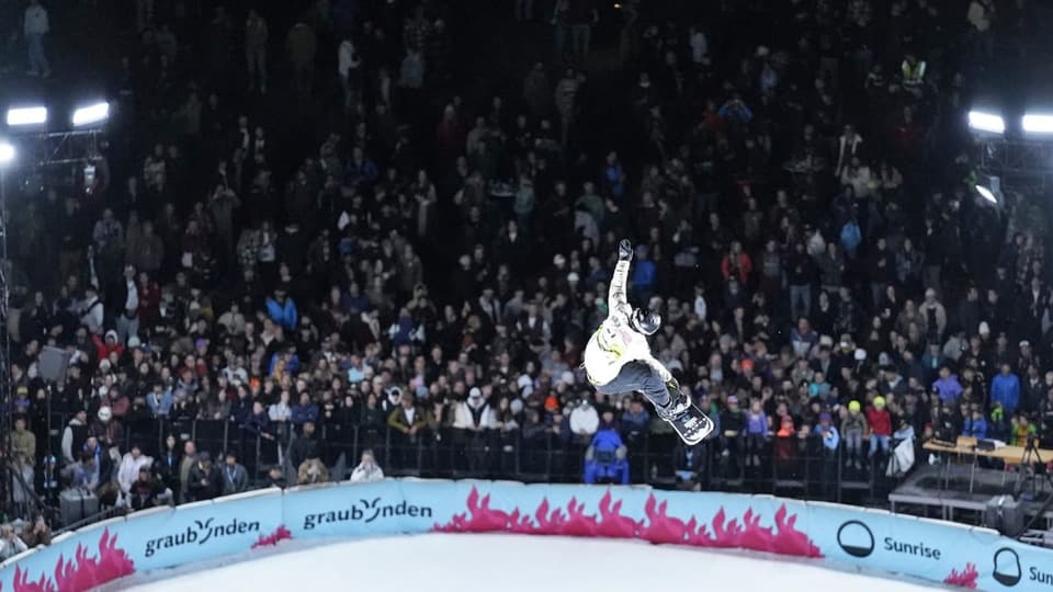 Snowboarder macht vor Publikum einen Trick in der Luft.