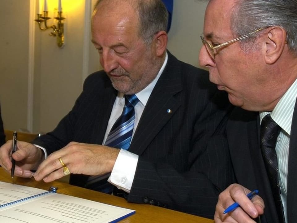 Die beiden Männer unterzeichnen den Vertrag.