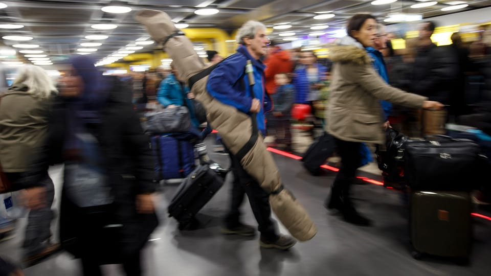 Touristen mit Skisäcken und Rollkoffern ziehen ihr Gepäck über den Genfer Flughafen.