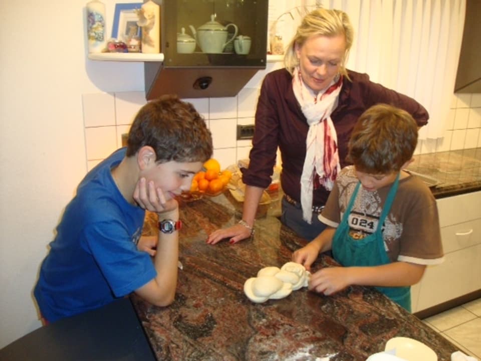 Antje Skodock mit den Kindern Nicola und Daniele am Zopf flechten. Sie erklärt auf Deutsch, wie es geht.