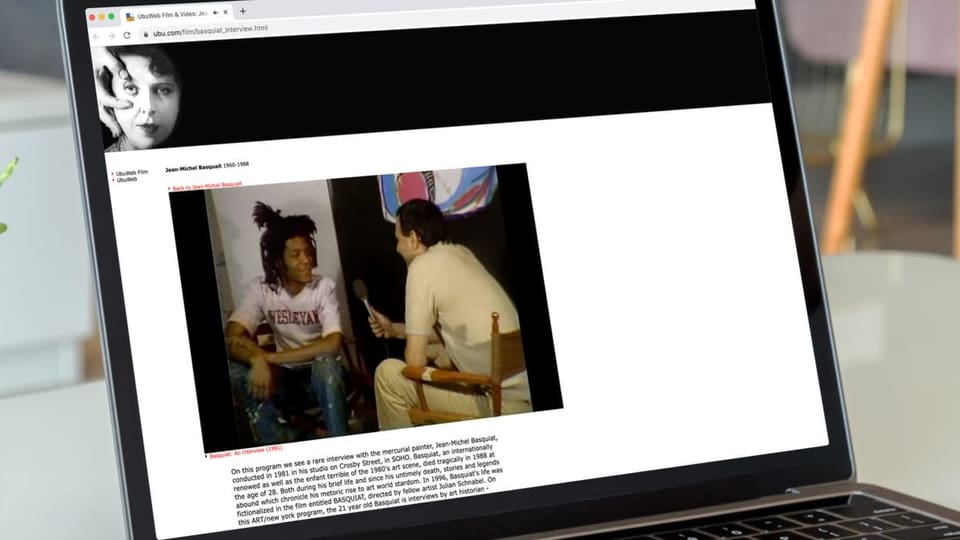 Foto eines Laptop-Bildschirms: Darauf ein Foto eines jungen Afroamerikaners im Gespräch mit einem Mann mit Mikrofon