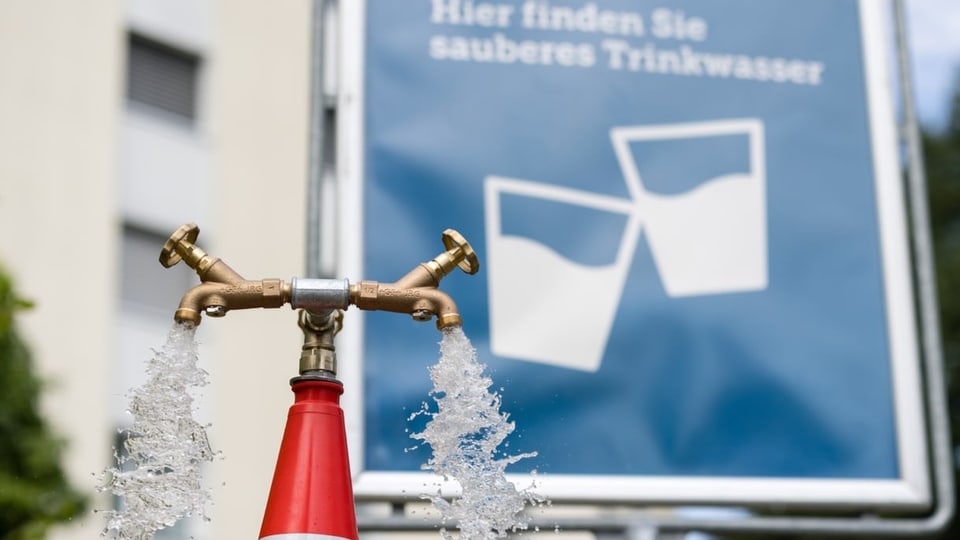 Aus der Wasser-Zapfsäule spritzt Wasser – dahinter ein Plakat mit der Aufschrift «Hier finden Sie sauberes Trinkwasser»